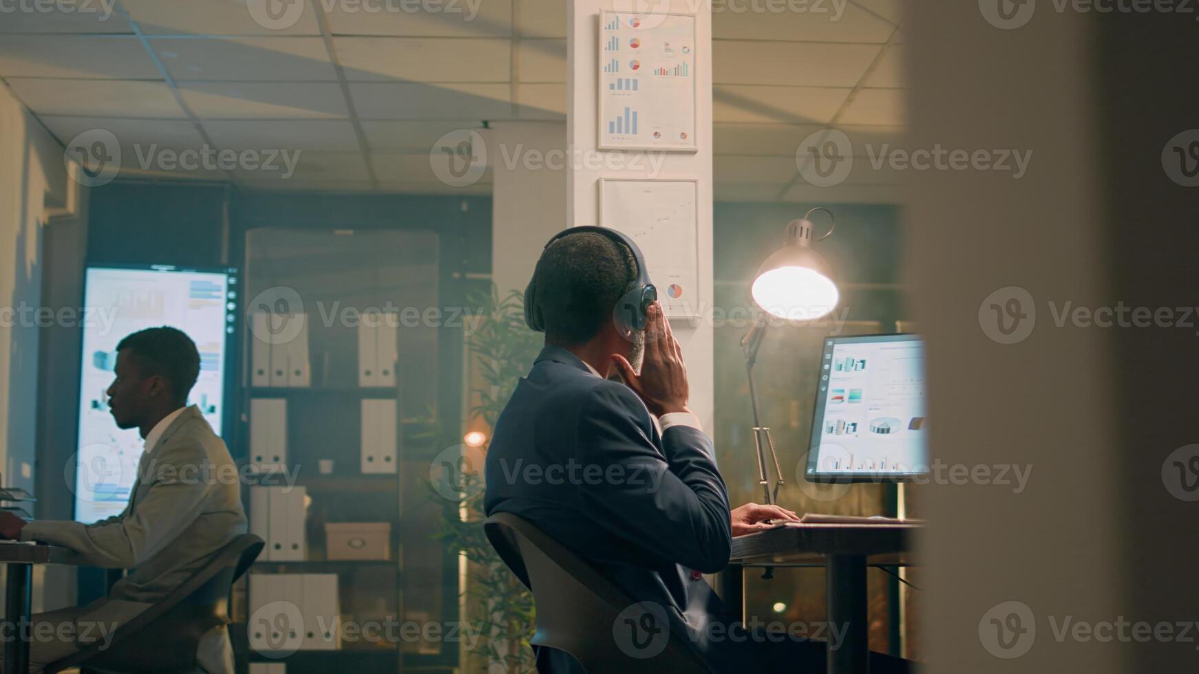 African american businessman enjoying music while checking statistical graphs on computer. Relaxed employee with headphones on solving project tasks in office during nightshift photo