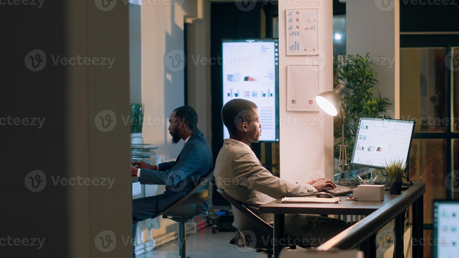 African american supervisor asking accountant to show him business project tasks progress in modern office during nightshift. Management executive overseeing employee working on computer photo