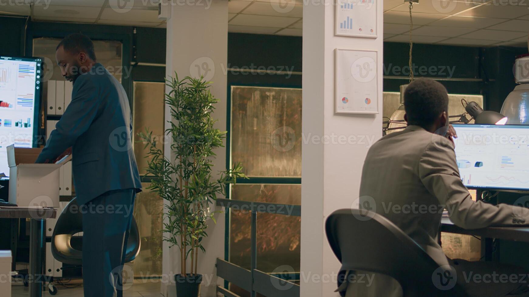 Upset worker holding box filled with desk belongings bidding farewell to colleague during last nightshift in office after being laid off. Sad businessman getting consoled after being fired from job photo