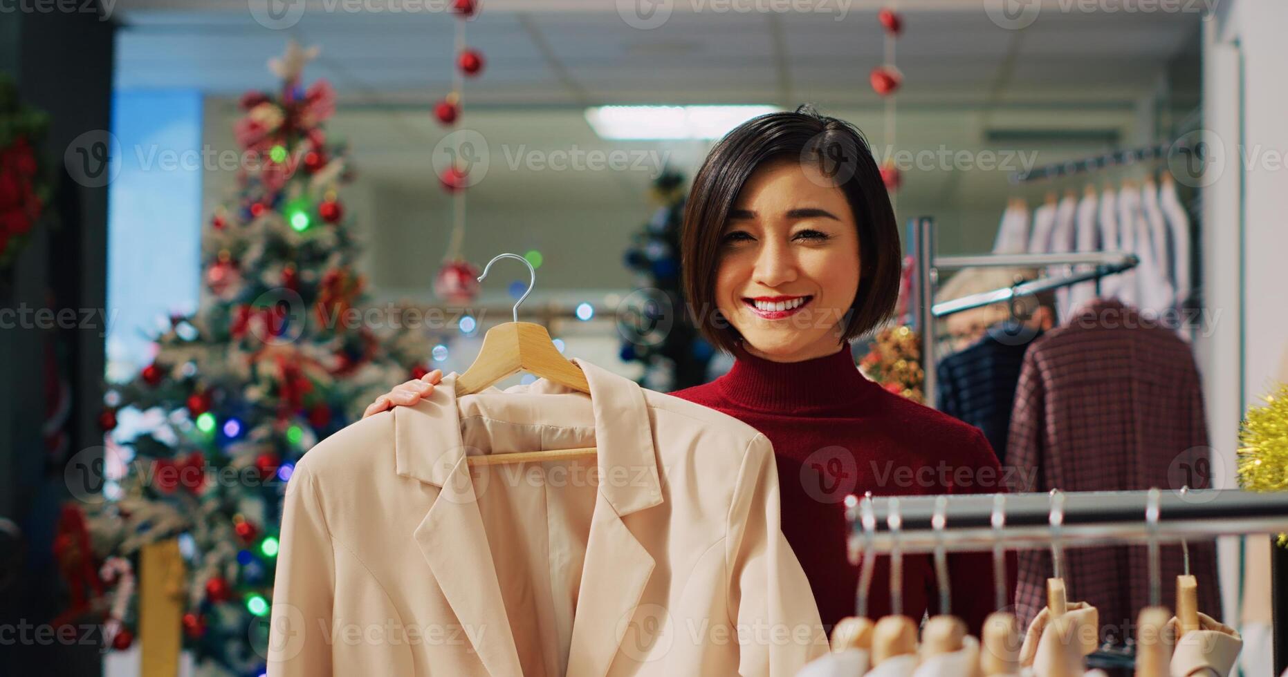 Portrait of happy woman browsing through elegant blazers on racks in Christmas adorn clothing store during winter holiday season. Smiling client checking fashion boutique items photo