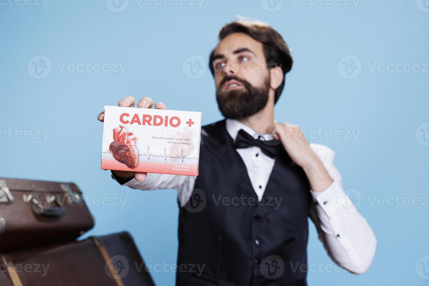 Hotel concierge presents cardiac pills in front of studio camera, recommending medication for heart disease or problems. Young man doorkeeper shows box of medicaments treatment. photo