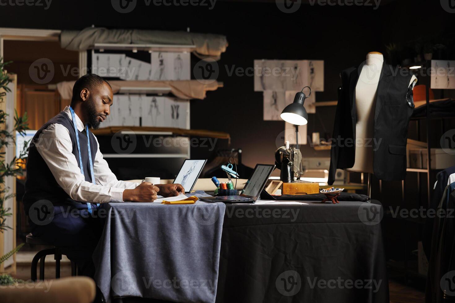 Relaxed couturier meticulously sketching upcoming stylish custom made fashion collection. Skilled tailor in atelier studio workshop creating stylish garments, surrounded by sewing materials photo