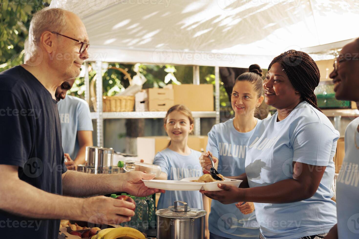 People from diverse backgrounds helping those in need by donating free food outdoors. Charitable group supports the hungry and less fortunate, serving meals and offering humanitarian aid. photo