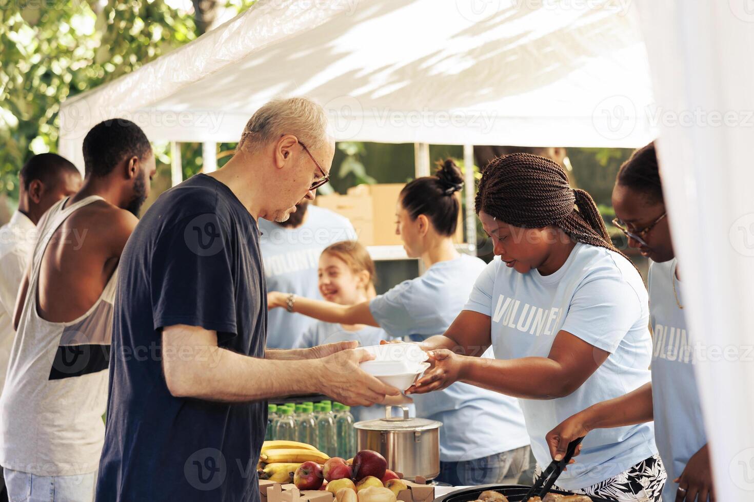 Young volunteers at local center giving complimentary nourishment to diverse group of homeless people benefiting from charitable food campaign. Charity workers share free meals to the hungry and poor. photo