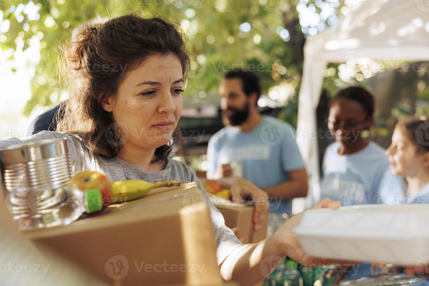Volunteers hand out packages and meal boxes offering free food to the homeless and needy. Close-up of underprivileged caucasian woman receiving hunger relief donation package from charity workers. photo