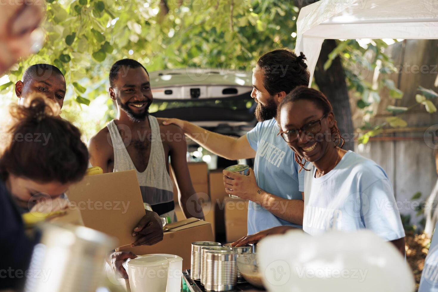 African American woman and caucasian man smile while providing boxes of canned goods handing out donation boxes to needy. Individuals volunteering by sharing necessities to poor and homeless people. photo