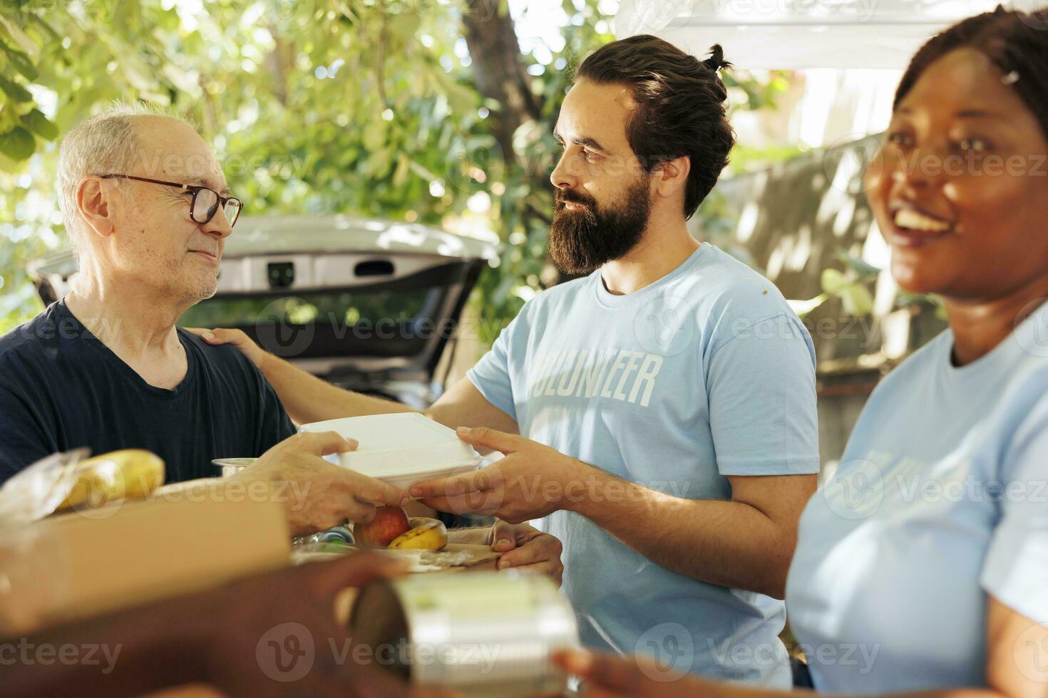 Close-up of multiethnic volunteers, including a smiling woman, distribute donations of food to the needy, offering help and hope to homeless people. Caring charity workers aiding the less privileged. photo