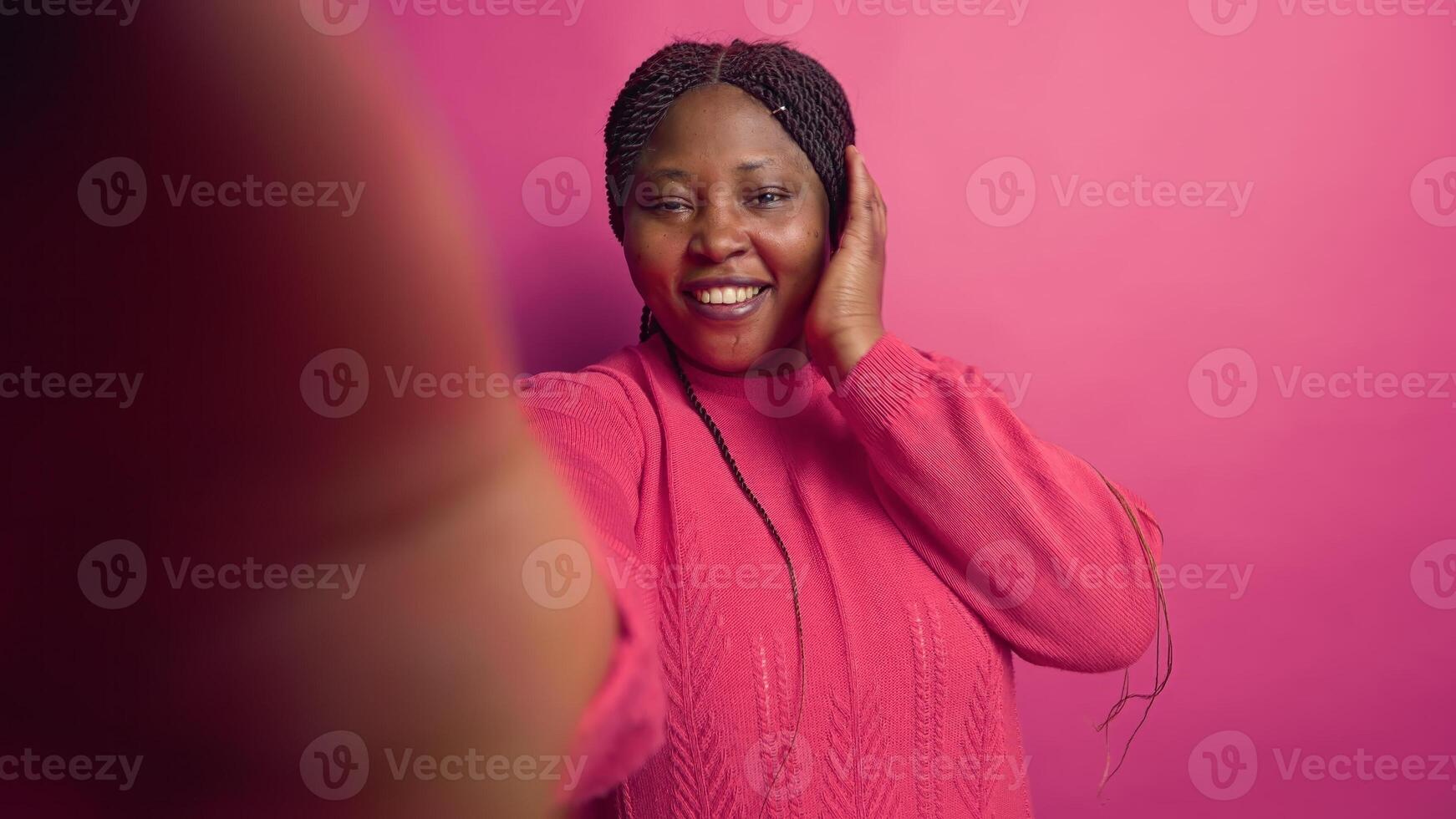 African american female vlogger talking on online video call with webcam, grasping smartphone. Enthusiastic black woman doing vlog content with digital mobile phone against vibrant pink background. photo