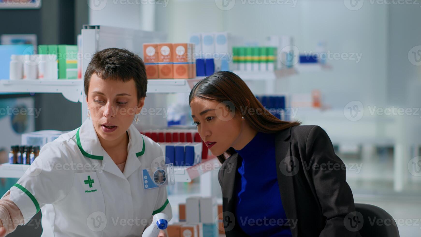Experienced chemist in pharmacy using electronic thermometer on asian woman, checking temperature. Patient and healthcare practitioner during routine checkup, monitoring flu symptoms such as fever photo