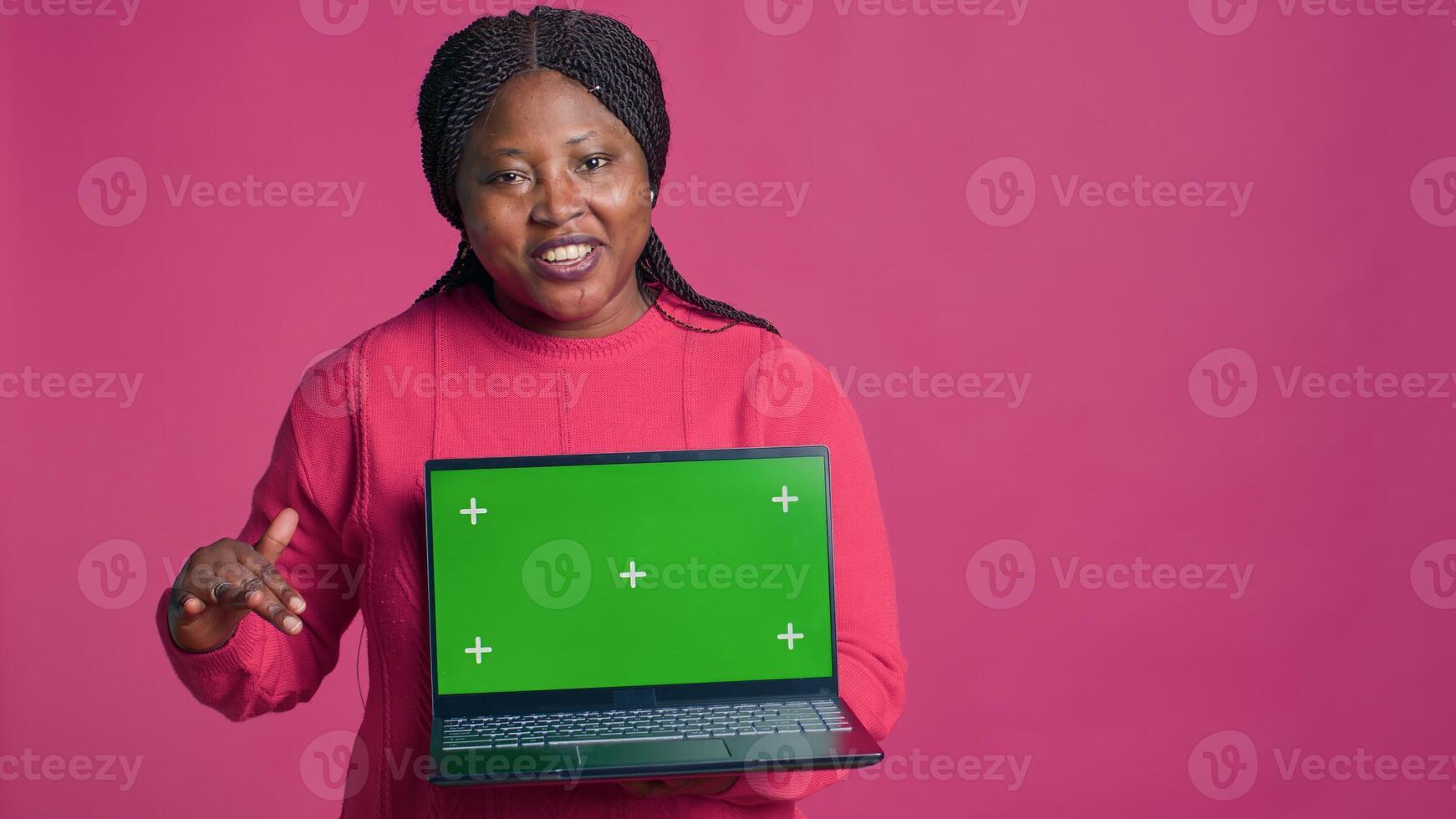 Young lady with african american ethnicity grasping laptop showcasing isolated chromakey template. Minicomputer with mockup green screen display held by beautiful black woman. photo