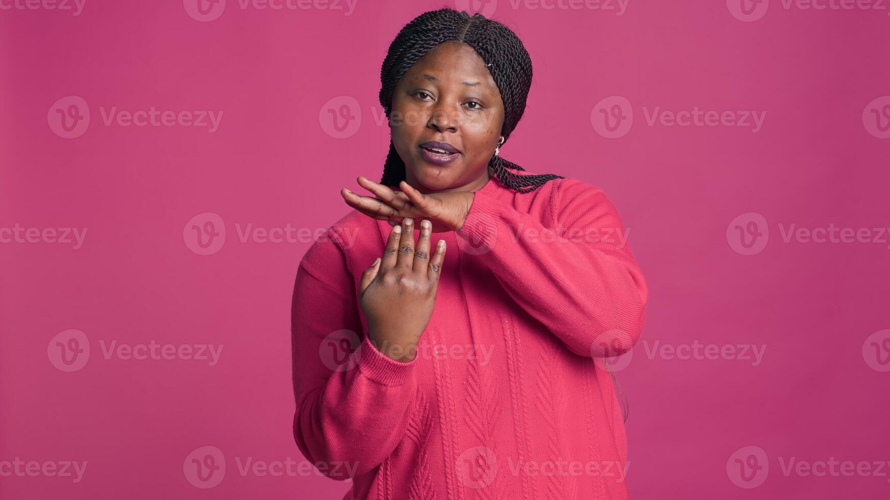 Expressive young black woman showing time-out sign using her hands in front of pink background. African american beauty displaying pause-break signal with body language towards camera. photo