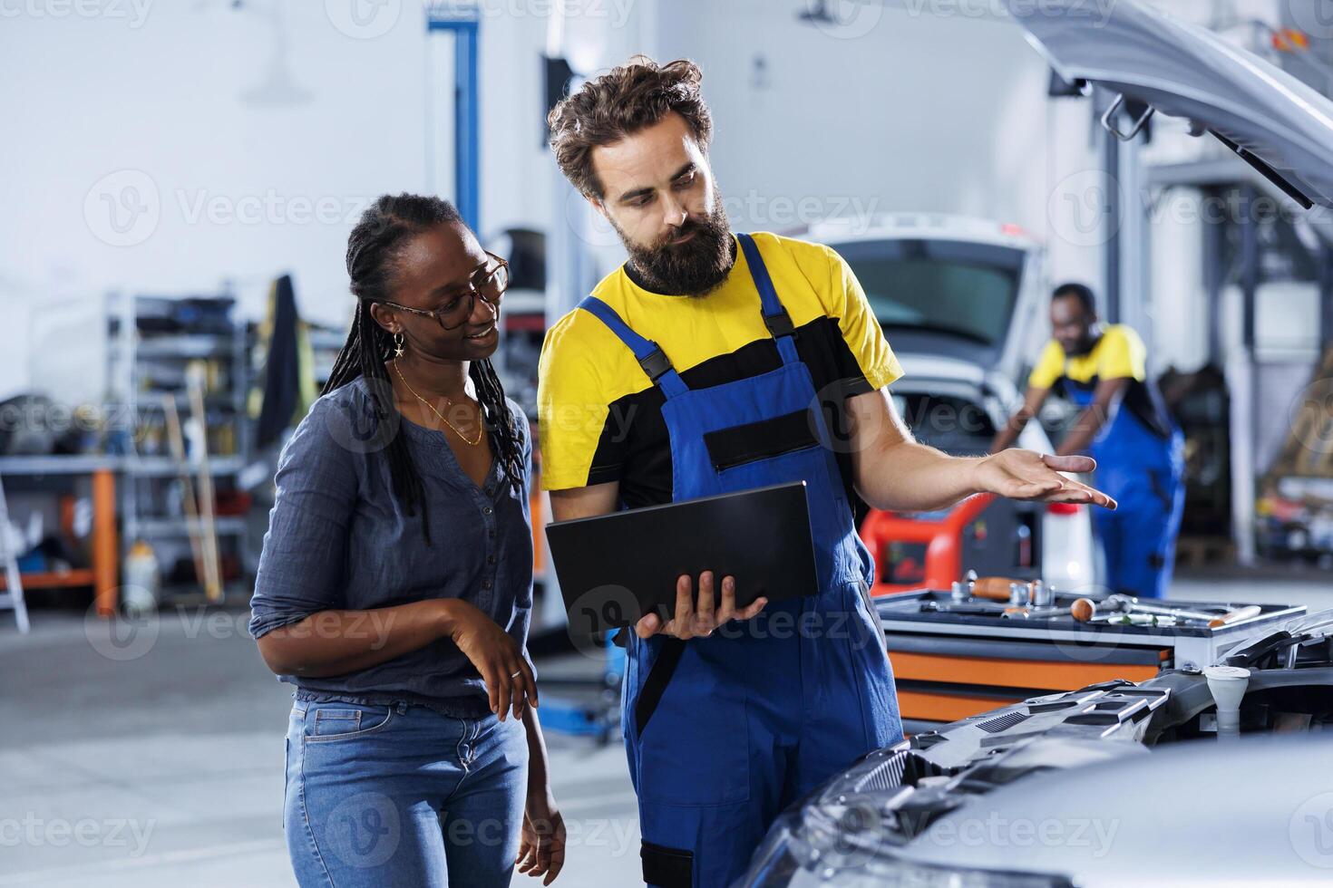 Mechanic at auto repair shop conducts annual vehicle checkup, informing customer about needed radiator replacement. Knowledgeable garage worker talks with customer after finishing car inspection photo