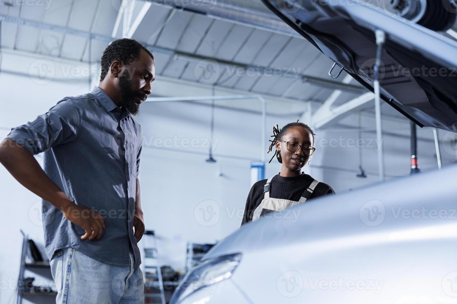 Mechanic at auto repair shop conducts annual vehicle checkup, informing customer about needed steering mechanism replacement. Competent garage worker talks with customer after finishing car inspection photo