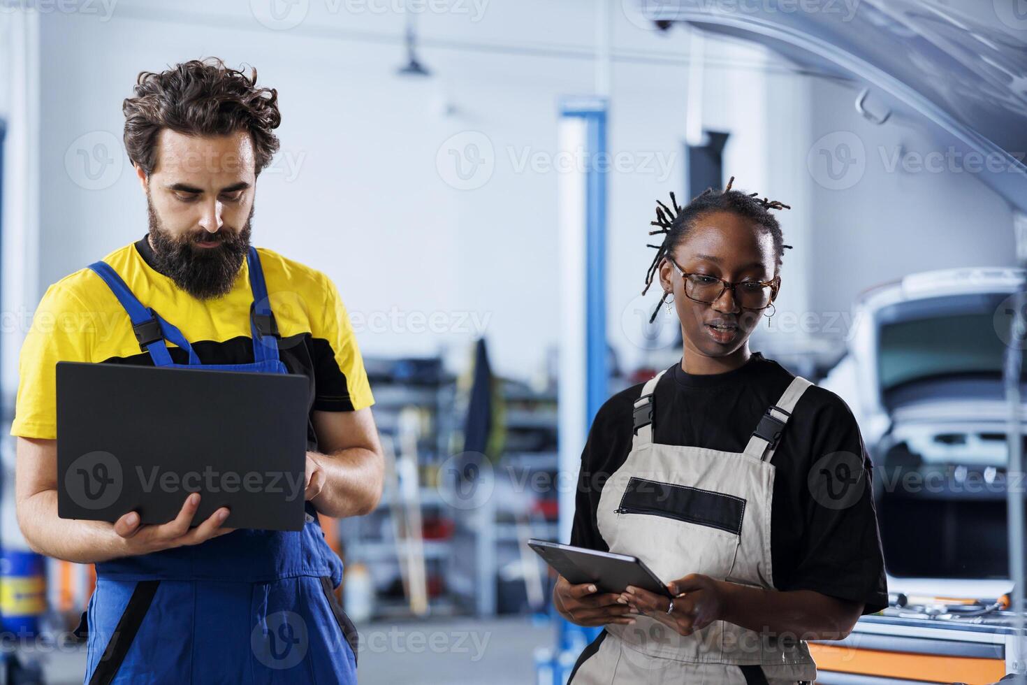 Engineer servicing broken vehicle, checking for damaged brakes under manager supervision. Teamworking employees in auto repair shop working together on fixing automobile, discussing best options photo