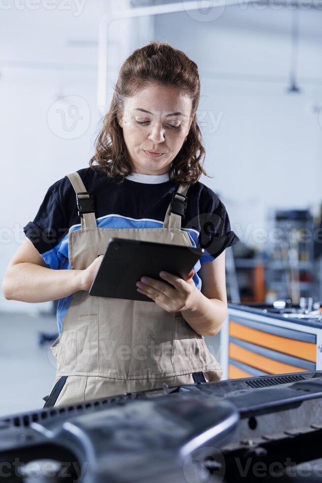 Diligent serviceman in car service orders new engine for damaged vehicle using tablet. Expert looking online for components to replace old ones in malfunctioning automobile photo
