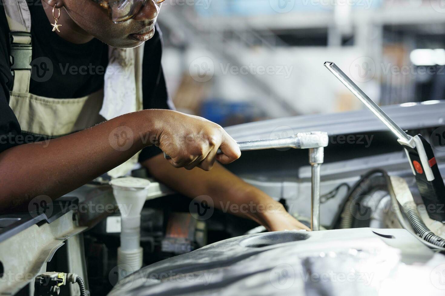 africano americano mujer en coche Servicio utilizando profesional mecánico herramienta a reparar roto batería. experto mecánico en garaje fijación cliente automóvil, asegurando óptimo automotor actuación foto