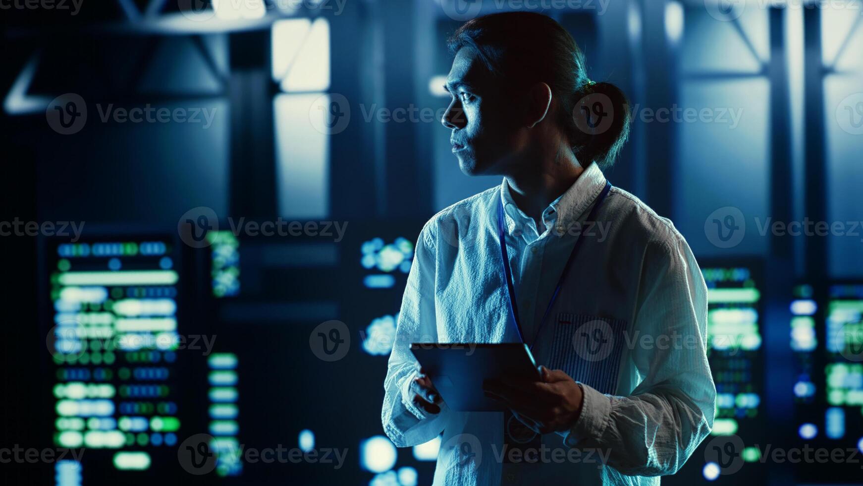 Asian employee walking through data center equipment clusters providing processing resources for different workloads. Productive engineer examining server rigs tasked with solving complex operations photo