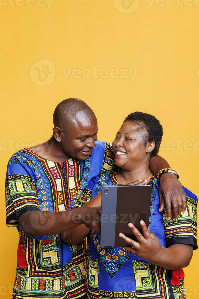 contento africano americano Pareja en amor abrazando mientras utilizando digital tableta juntos. alegre maduro novio y Novia tocando en dispositivo pantalla táctil y desplazamiento Internet página foto