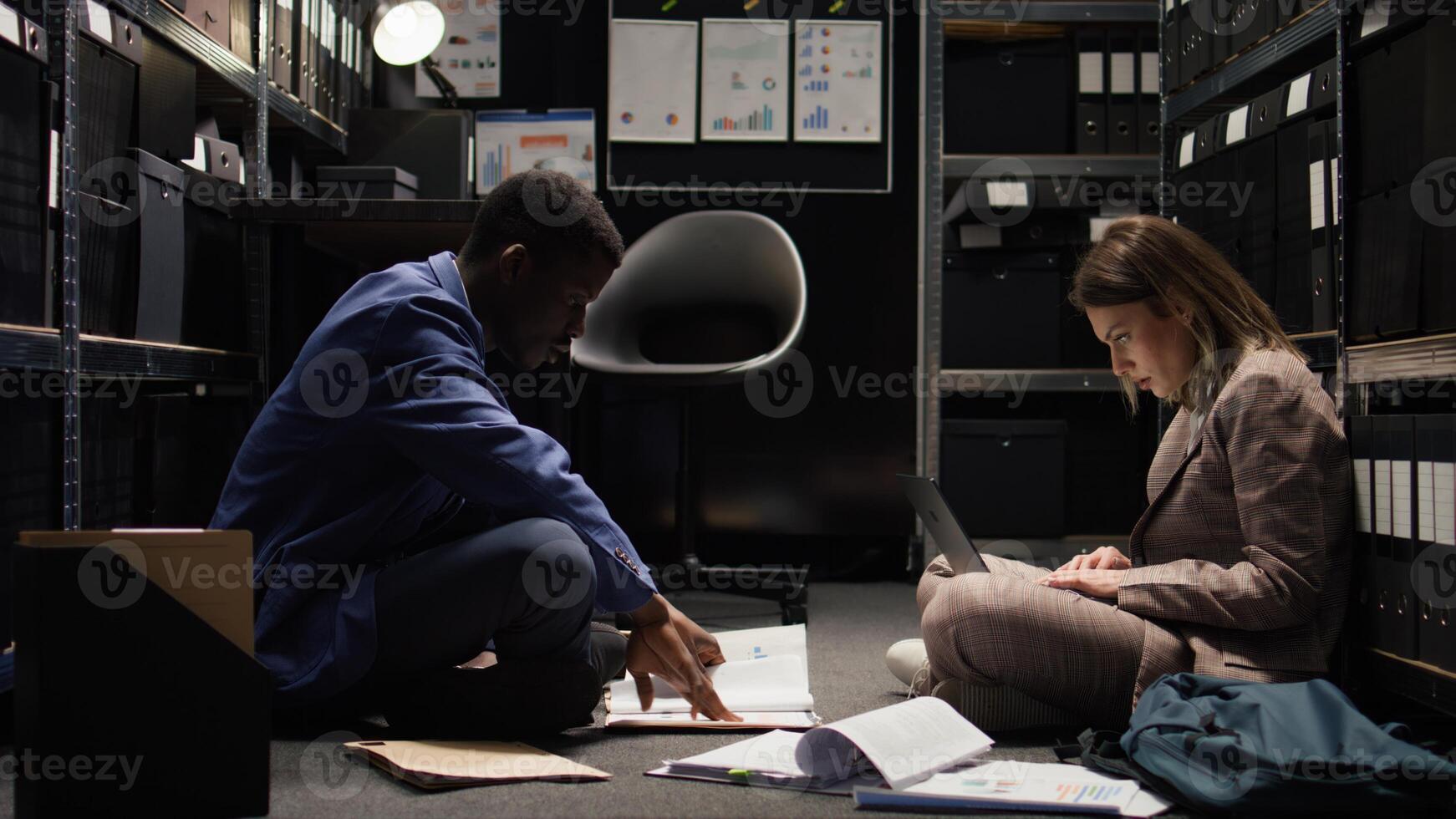 African american investigator assists with case files in evidence room as policewoman searches online for criminal records on laptop. Private detective thrilled to provide important information. photo