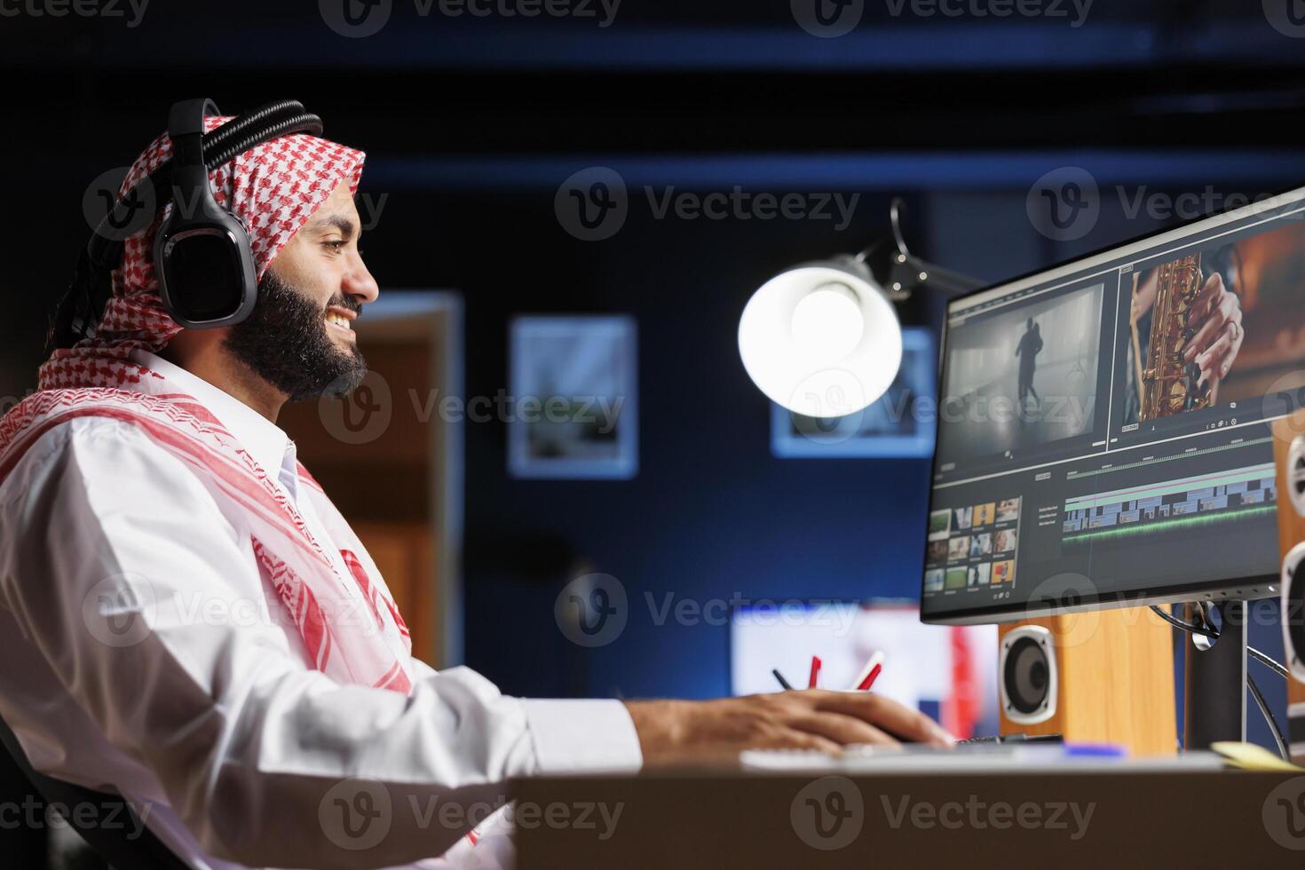 Middle Eastern employee editing video content on multimedia software seen on his computer screen. Side-view shot of male filmmaker working on movie montage edit on the pc monitor. photo