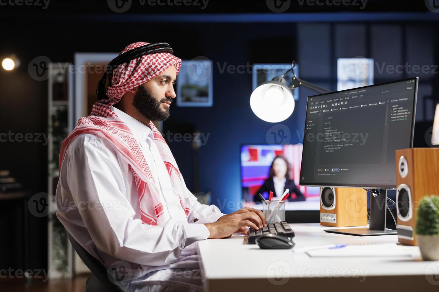 Side-view of Muslim developer writing code on desktop pc, parsing algorithm in a software agency. Using a computer monitor, a Middle Eastern male coder works on a user interface. photo