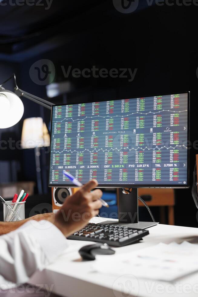 This image shows a pc monitor displaying financial reports while a businessman writes down notes. Detailed view of the computer screen having research and statistics information. photo