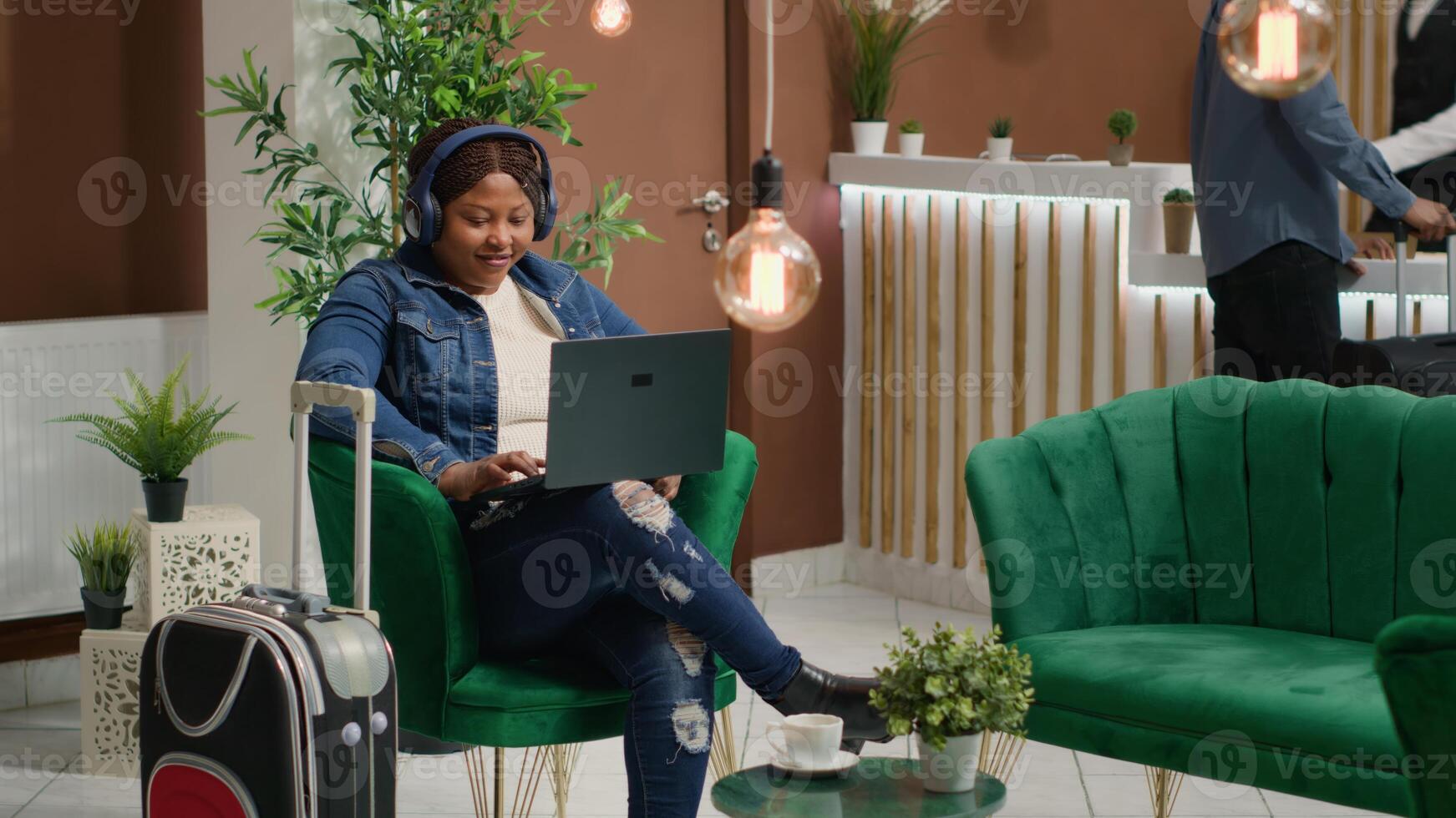 Traveller watches tv show in lounge area, waiting to do check in procedure after long flight. African american woman using laptop in hotel lobby, passig time before registering at front desk. photo