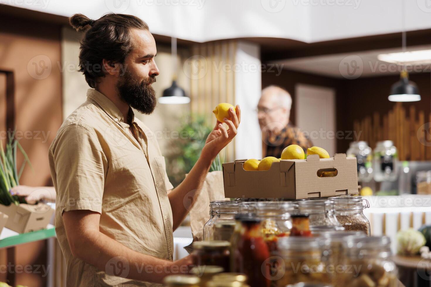 Man in zero waste store taking time to analyze fruits, making sure they are handpicked and farm grown. Green living customer thoroughly checking local supermarket food items are ethically sourced photo