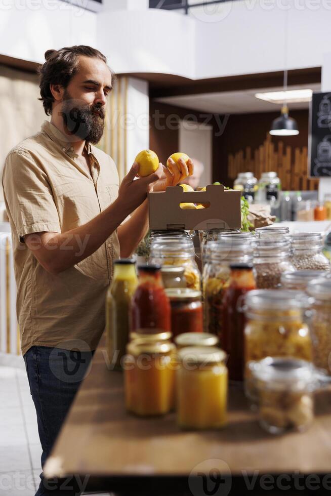 Green living man purchasing locally grown lemons in sustainable zero waste supermarket. Customer happy to find eco friendly chemicals free organic fruits in local neighborhood store photo