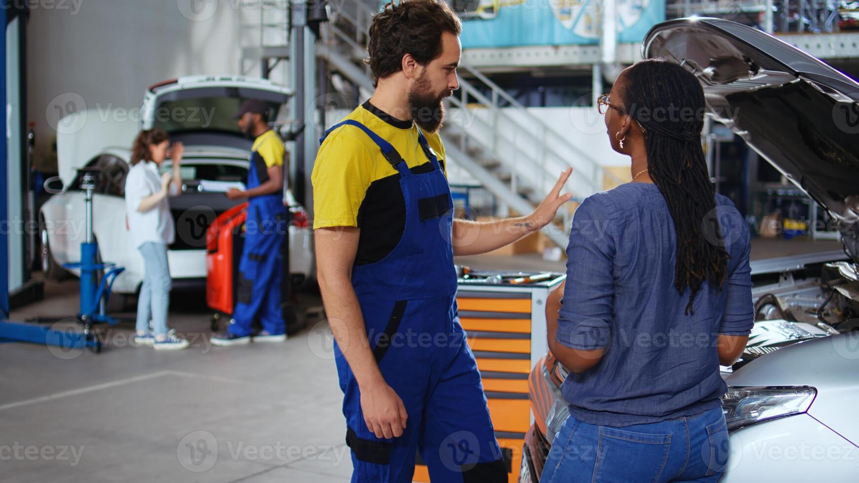 Teamworking colleagues in garage workspace fixing car for customers, thoroughly checking underneath vehicle hood. Mechanics doing routine maintenance on automobile in auto repair shop photo