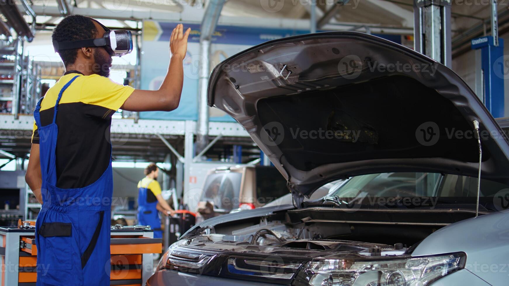 African american repairman employee in garage uses simulating virtual reality glasses to visualize car components in order to fix them. Mechanic wears vr headset while working on out of order vehicle photo