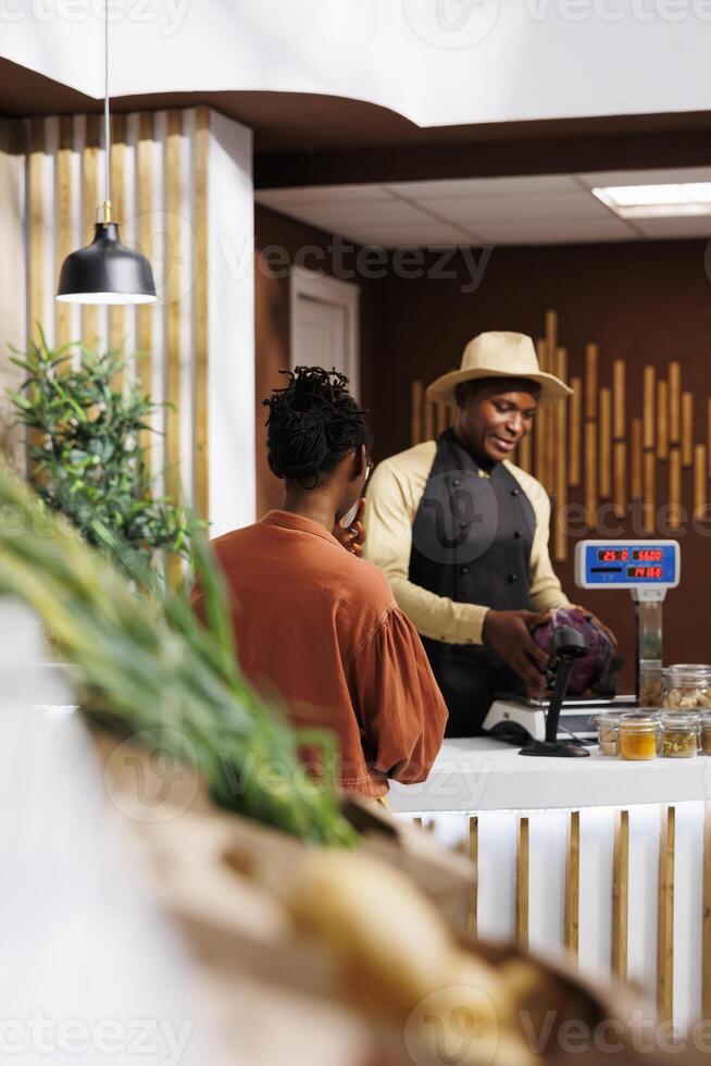 While shopping for fresh products, a black woman is helped by a male vendor. The shopkeeper provides a choice of vivid and healthful alternatives, resulting in a pleasant shopping experience. photo