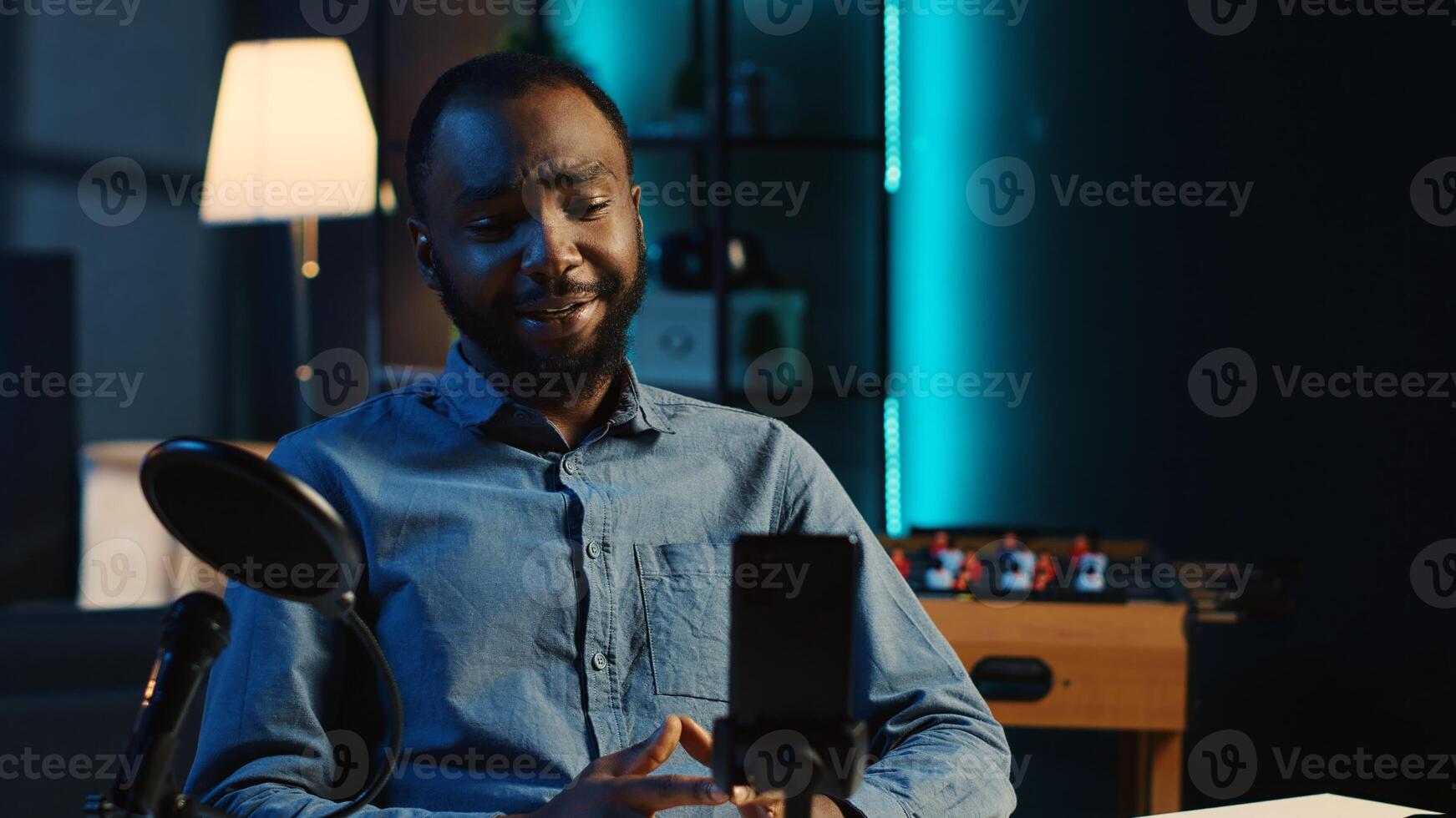 Content creator arriving in dimly lit studio, using smartphone camera to record video intro for online streaming platforms. Influencer greets fanbase, using mobile phone to capture footage photo