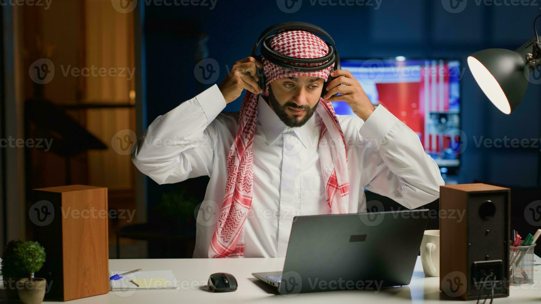 Arab man with wireless headphones enthusiastic about working from home. Cheerful Muslim businessman doing online research while listening to music to make time pass faster photo