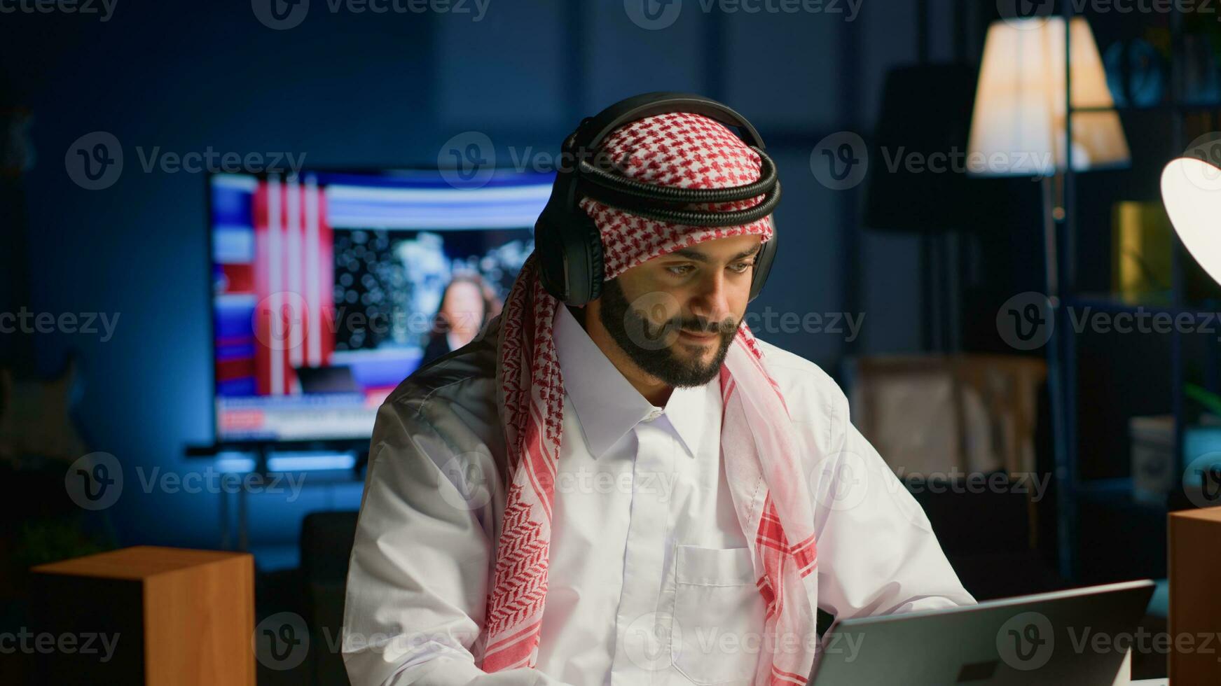 Arab worker with wireless headphones enthusiastic about working from home office. Cheerful Middle Eastern businessman doing online research while listening to music to make time pass faster photo