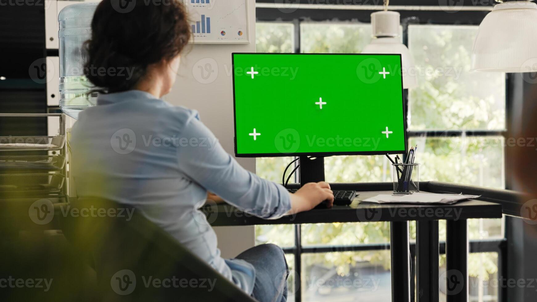 Specialist watches greenscreen desktop sitting at office desk, checking blank chromakey display on monitor. Woman typing information and looking at isolated mockup layout on computer. photo