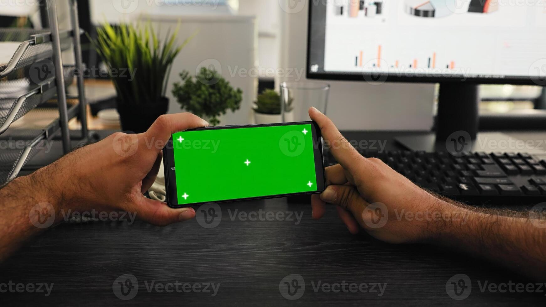 POV of worker holds phone with greenscreen display at desk, working with isolated mockup template at workstation. Young employee looking at mobile phone screen with chromakey. photo