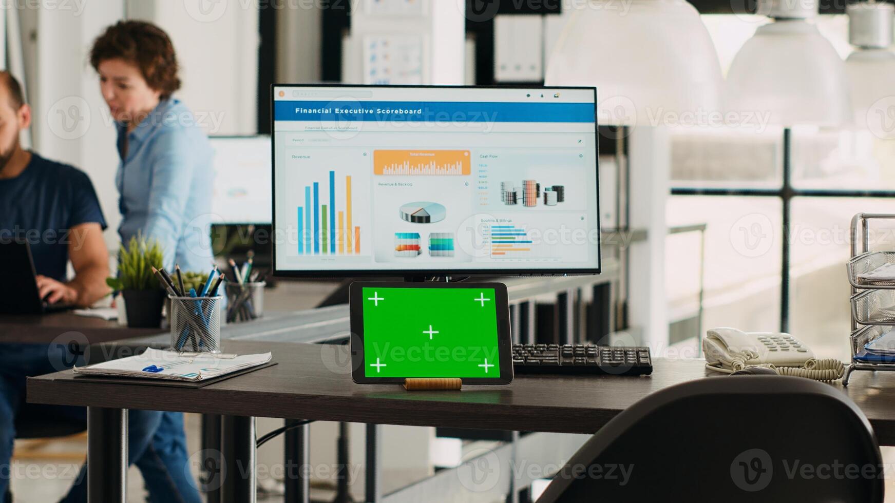 Desk with tablet showing greenscreen, empty workstation in creative agency coworking space. Modern gadget running isolated chromakey display in small business workplace, mockup screen. photo