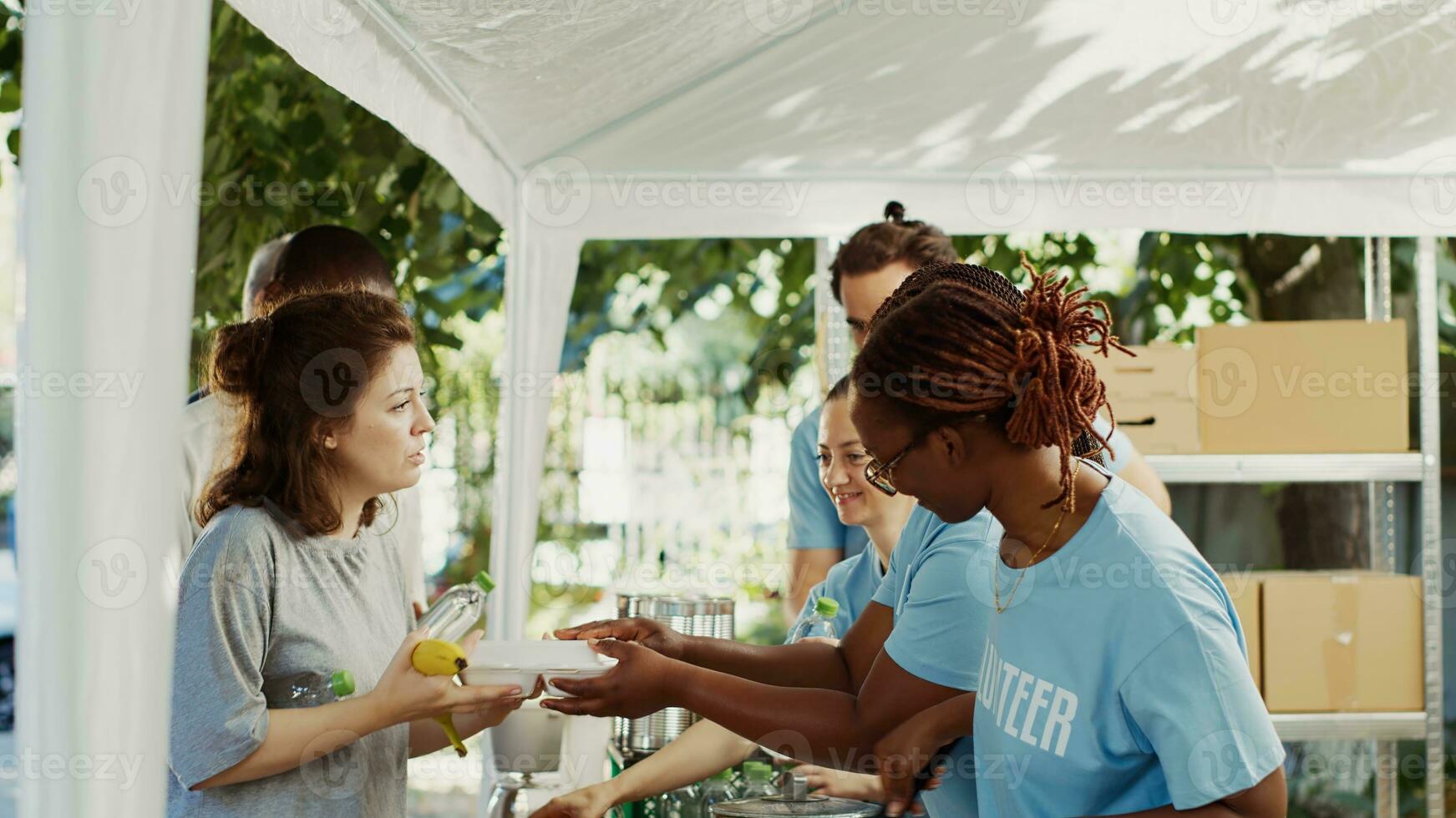 Young African American and Caucasian volunteers handing out free food and necessities to the less poor. At a homeless shelter, friendly charity workers give hunger relief and humanitarian help. photo