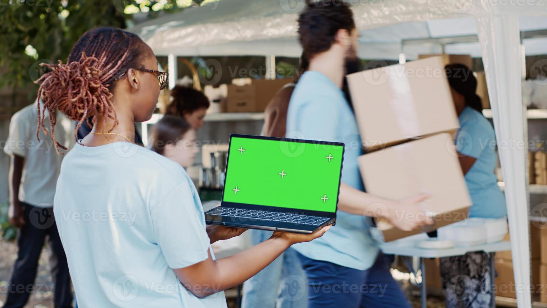 African american woman working for charity is shown holding laptop with blank chromakey template. Young black lady grasping wireless computer with isolated green screen for customization. photo