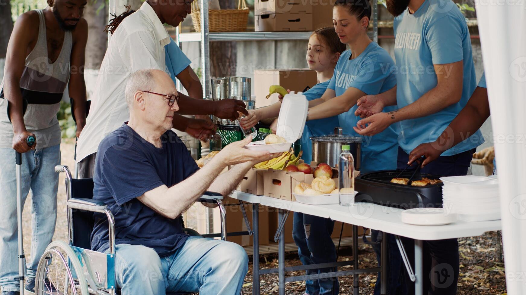 The needy are helped and fed by charitable group, and homeless people are given free food, including fresh fruit. Wheelchair-bound disabled man is given a warm meal from volunteer at a food drive. photo