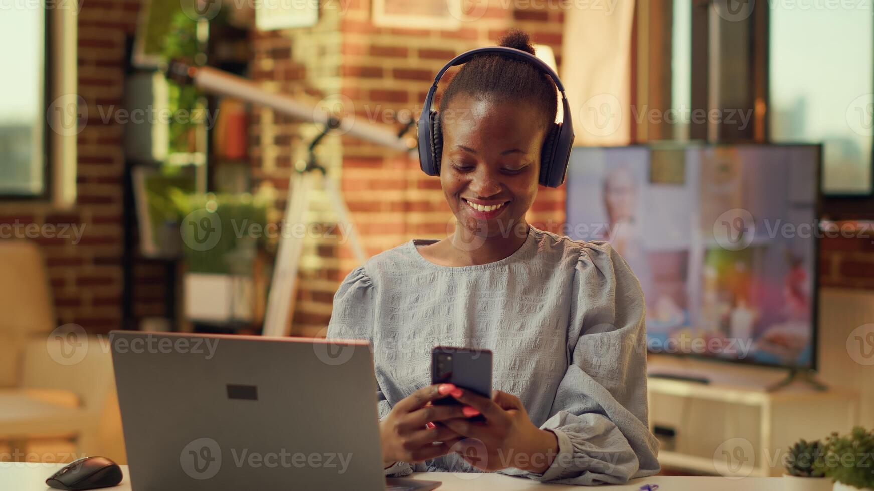 Teleworker browsing online site on phone, taking break from online freelancing tasks during sunset hour. African american person using smartphone social media app at home office. photo