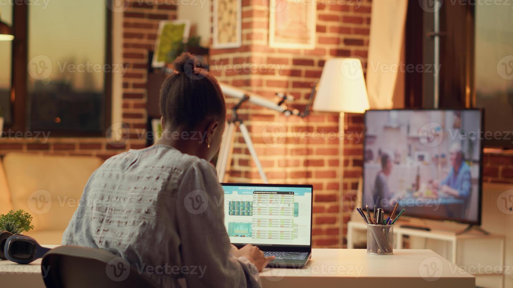 Freelancer studying data for research, preparing to solve new online tasks for marketing and sales segment. African american woman providing freelance services from home, sunset hour. photo