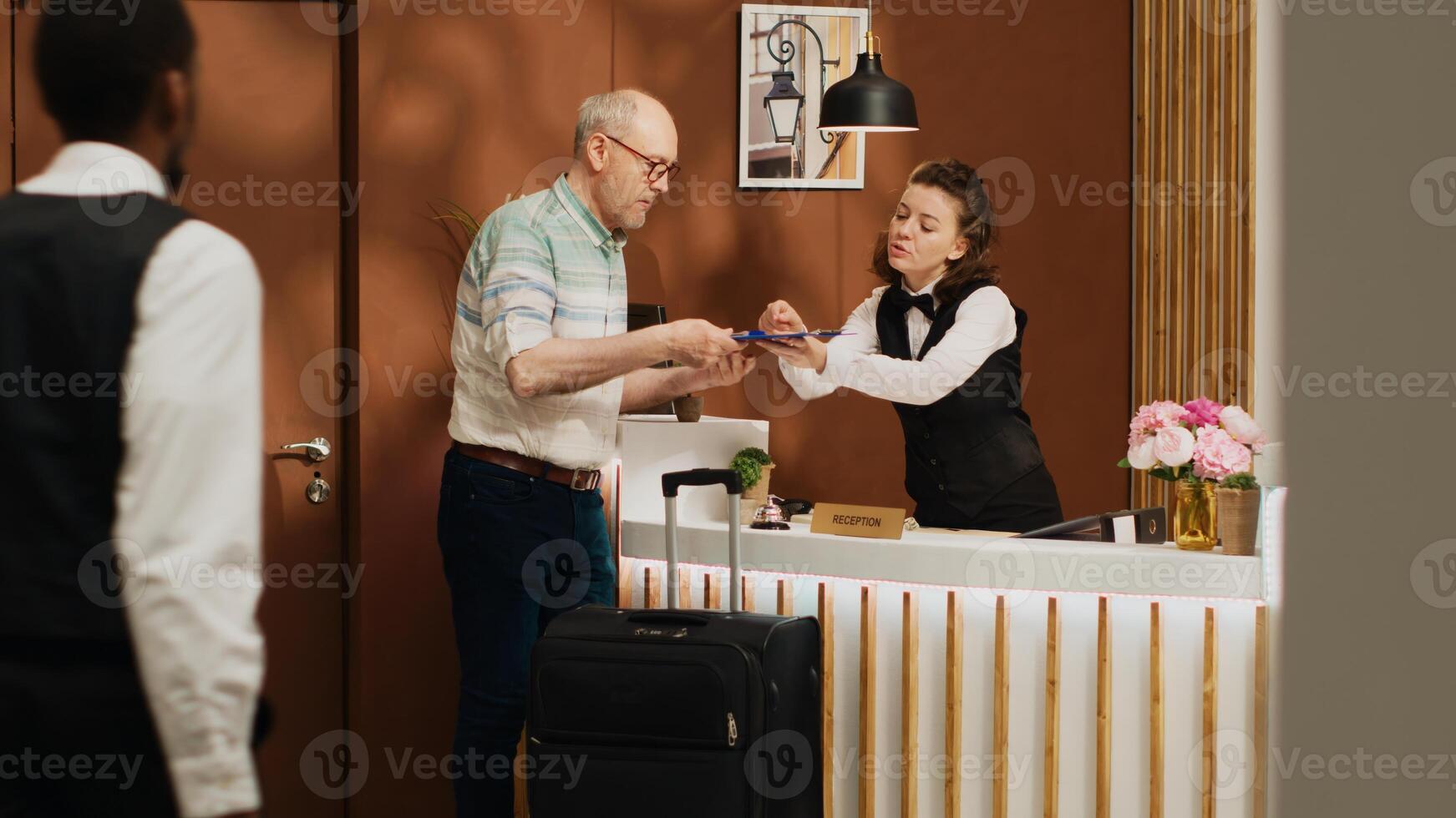 Senior guy at front desk doing check in routine in expensive five star hotel lobby. Traveller signing registration forms at front desk, checking room service and ammenities on holiday trip. photo