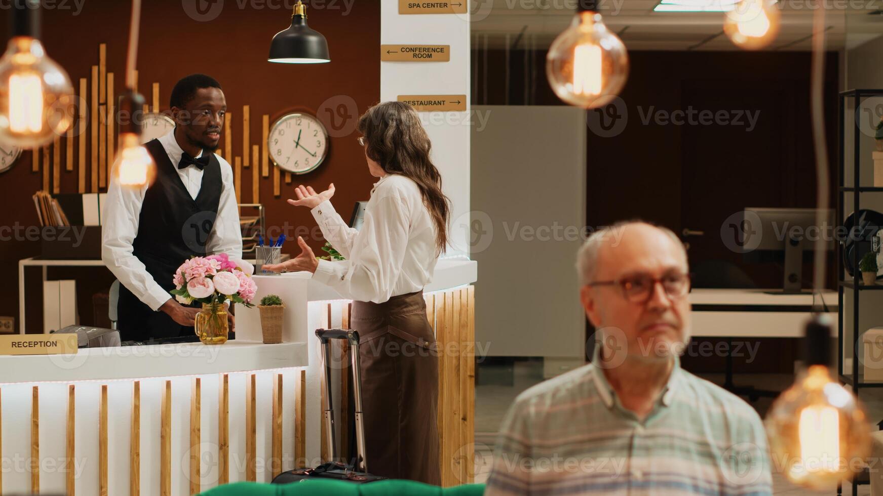 Retired adult at front desk does check in process in luxury hotel lobby. Reception staff assisting traveller with registration to ensure pleasant stay, all inclusive room accommodation. photo