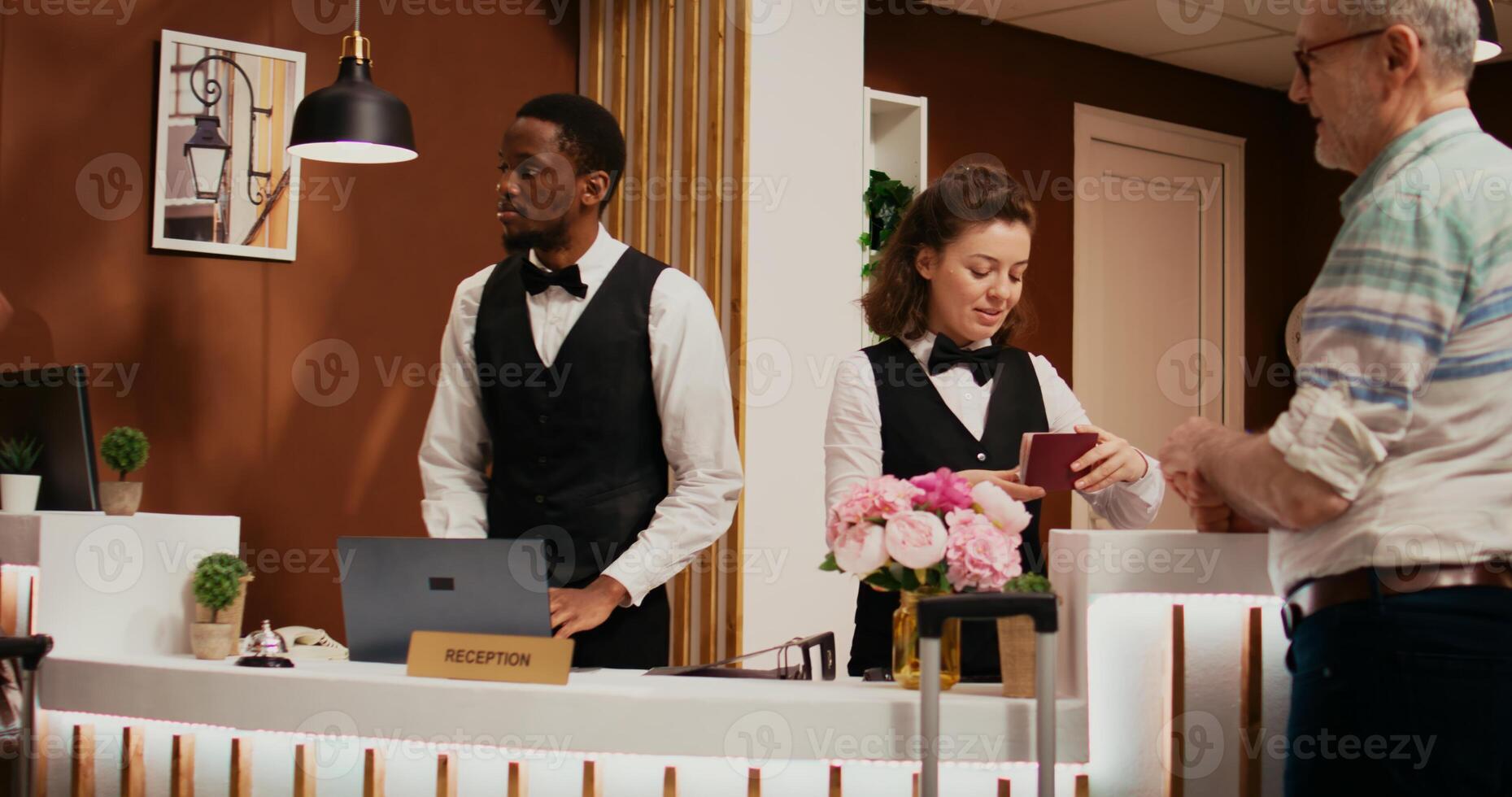 Front desk staff checking passports for tourists with room reservation at five star hotel, looking at id documents in reception lobby. Diverse employees assisting senior couple. photo