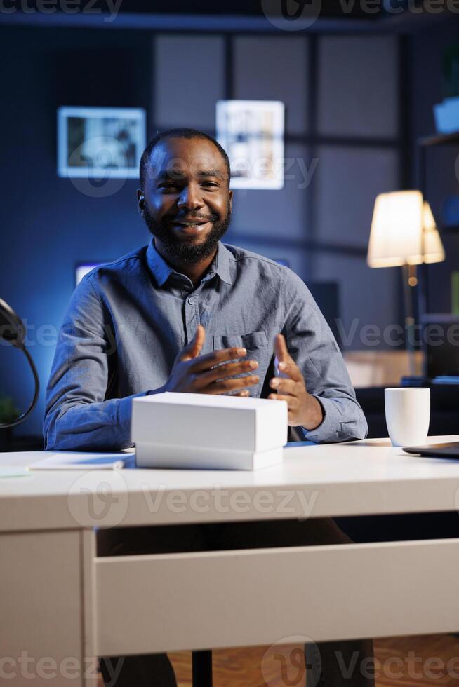 Cheerful content creator with product waiting to be unboxed in front of him while he does video introduction. Viral influencer doing unboxing footage for his internet fanbase photo