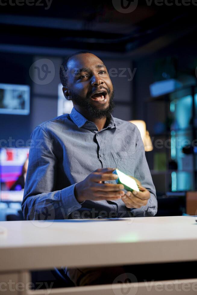 Influencer in studio using camera to capture live broadcast, reviewing mini RGB lights. BIPOC online show host filming electronics haul, presenting wireless LED lighting device to viewers photo