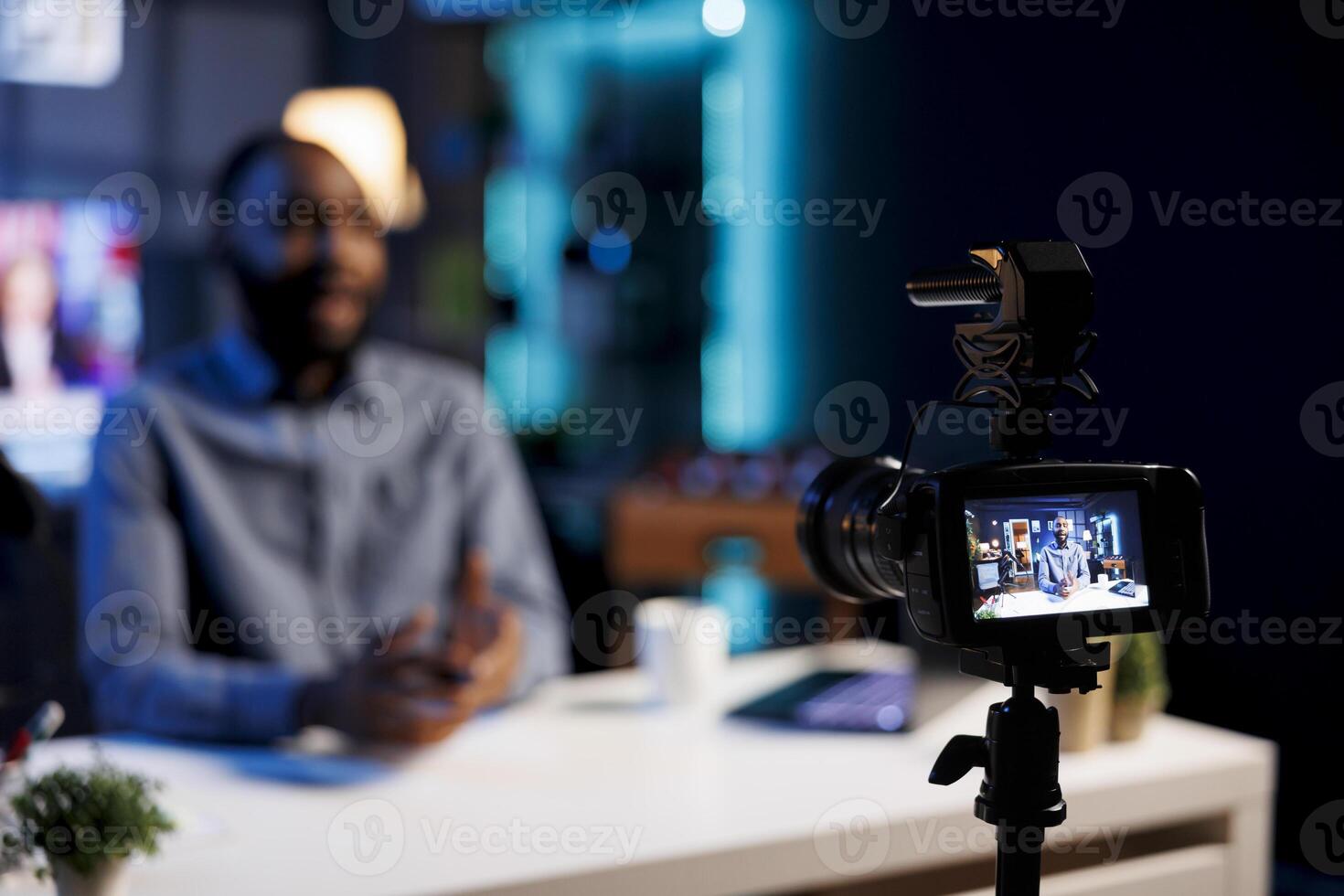 Focus on professional camera capturing footage of BIPOC man chatting with online audience. Viral content creator in blurry background talking with fans, filming with high quality recording tech photo