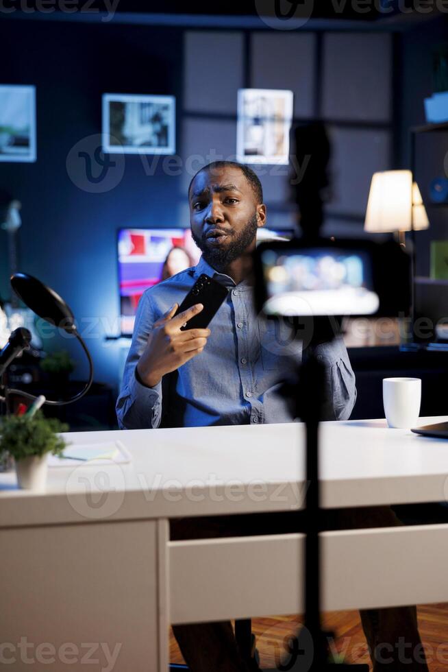 Excited content creator in studio films smartphone video review for tech enthusiasts. Trending phone engineer hosts technology internet show, unboxing newly released cellphone photo